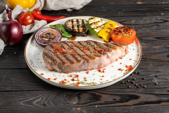 Rib Eye Steak With Grilled Vegetables. A Classic Hot Dish Of Premium Beef Steak (cowboy Ribeye Or Entrecote) With Eggplant, Zucchini, Peppers, Tomatoes And Onions On A Wooden Kitchen Table.