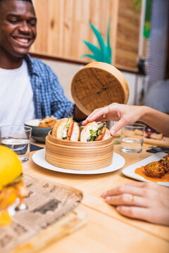 Crop smiling multiethnic friends gathering together at table in cafe and having dinner with tasty sandwiches