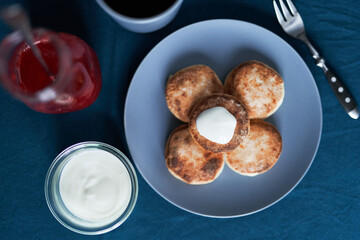 Cheese pancakes on a grey plate with sour cream and strawberry jam and black coffee with fork near it. Tasty breakfast concept