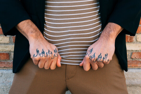 Crop unrecognizable male in stylish apparel demonstrating hands with tattoo near brick wall in town