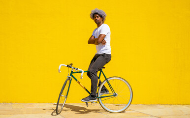 Afro black man doing a trick with his bike. Black biker concept. Black cyclist on a yellow background.