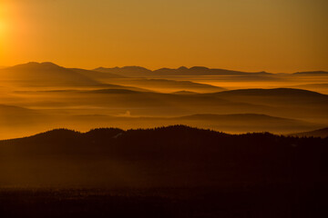 the sun sets below the horizon and illuminates the fog in the valley with a yellow light