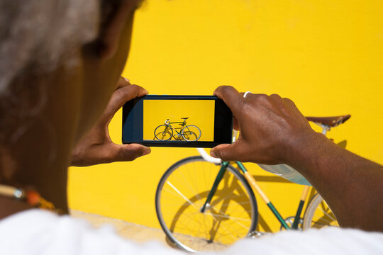 Black man taking a photo of his bike with the phone on a yellow background. Concept of selling online. Sell a bicycle.