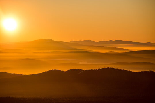 the sun sets below the horizon and illuminates the fog in the valley with a yellow light