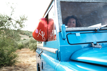 Low angle of vintage shiny car with red air balloons in shape of heart parked on sandy road in countryside