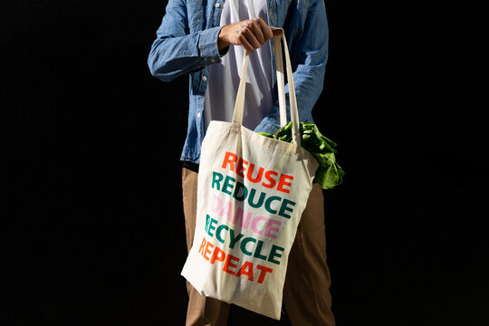 Crop anonymous male buyer holding fabric shopping bag with text message of reuse and recycle concept on black background