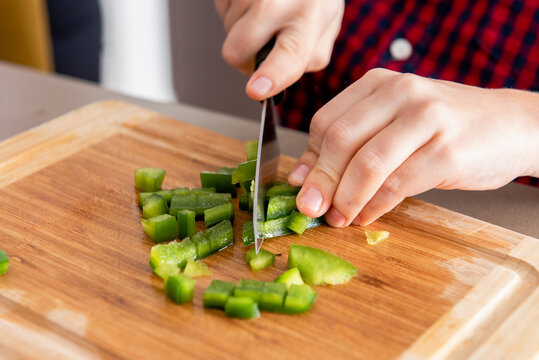 Crop cute little son cut capsicums while cooking with his mother in modern kitchen