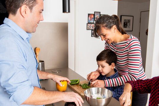 Cheerful family gathering in modern equipped kitchen while cutting vegetables and cooking lunch together