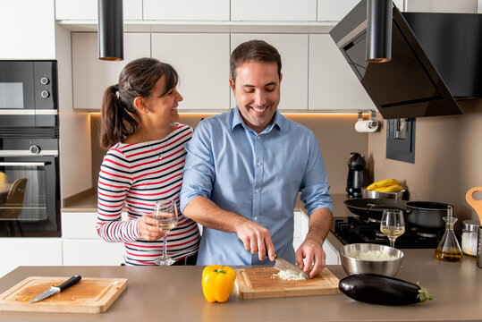 Happy smiling couple in casual clothes standing near kitchen counter and cutting onion while cooking lunch together