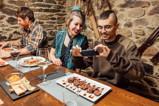 Cheerful friendly hipsters sitting together in cafe and taking picture of palatable meat slices served on plate with sauce