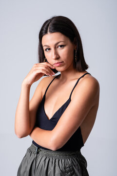 Beautiful female wearing black low neckline top standing against white background in studio and looking at camera
