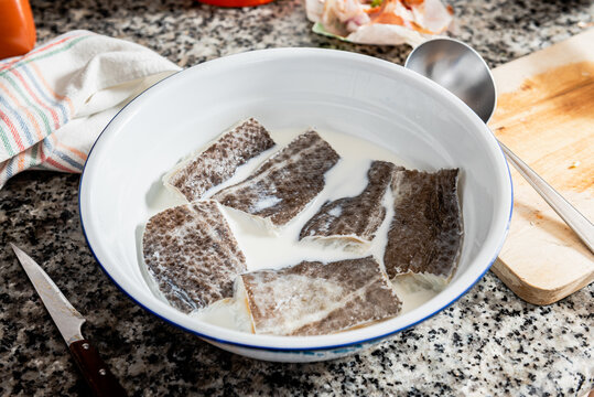 Salted cod fish steaks being soaked in milk before cooking during preparation of Catalan cod dish in home kitchen