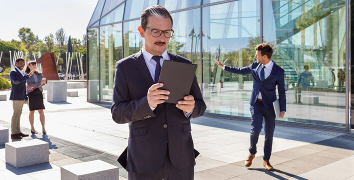 Serious middle aged male manager with mustache in classy outfit holding documents in hand and looking away while thinking about business strategy on street