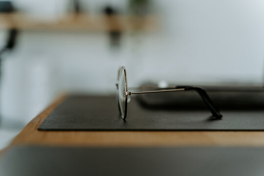 Classic eyeglasses of round shaped placed on black mat on blurred wooden desk