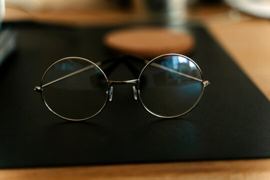 Classic eyeglasses of round shaped placed on black mat on blurred wooden desk