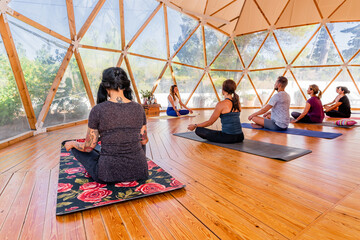 Back view of group of anonymous people sitting with crossed legs on mats on parquet while practicing yoga in class