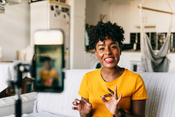 Cheerful young African American female blogger recording video on smartphone while preparing content for social networks at home
