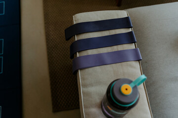 High angle collection of elastic bands of different resistance levels placed on cozy couch arm near water bottle before exercising