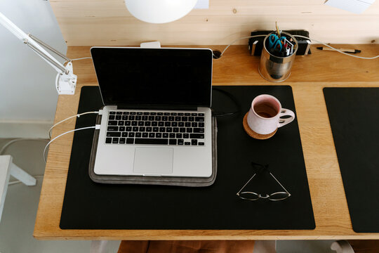 From above composition of modern portable netbook with black screen placed on wooden desk near cup and eyeglasses in light office