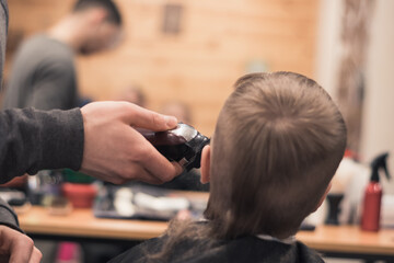 A pretty boy toddler happy to be on the haircut with a professional children's hairdresser. Blond little boy having a haircut at hair salon. Hairdresser's hands making hairstyle to child.