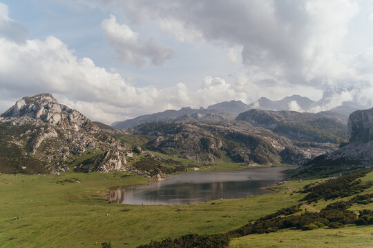 Amazing scenery of highland valley with abundant greenery and majestic rocky mountains surrounding tranquil pond
