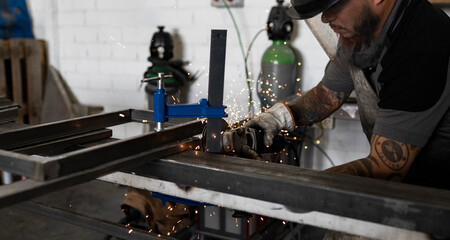 Side view of serious male welder using electric grinder and cutting metal detail in grungy workshop