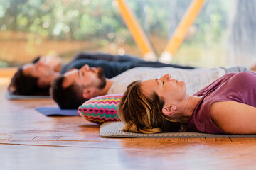 Side view of people with closed eyes lying on mats after practicing yoga on wooden floor in class