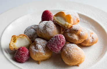 Presentation of delicious profiteroles with vanilla cream, strawberry and powdered sugar.