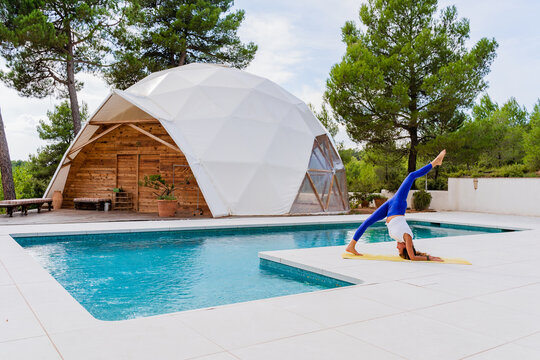Side view of unrecognizable flexible barefoot female in sportswear standing ion yoga pose near swimming pool