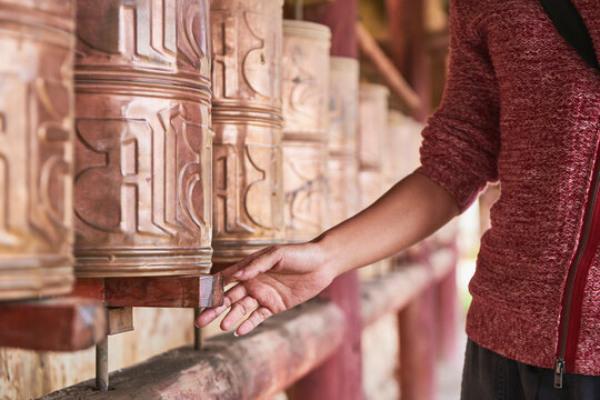 Full body of Asian female passing by Tibetan rolls with ancient prayer near sacred oriental temple