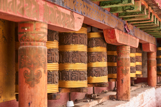 Exterior of Tibetan church decorated with big cylindrical rolls with stripes and hieroglyphs between red shabby columns