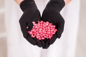 Wax pellets in the hands. Pink wax for depilation close-up in the hands of gloved hands.