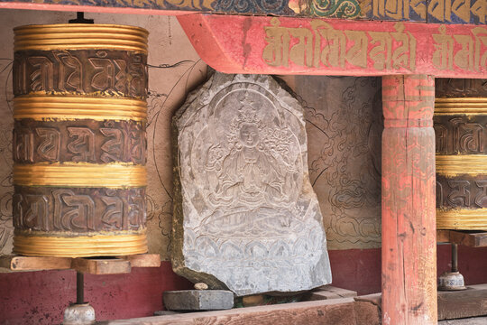 Piece of stone with image of Buddha engraved on surface between Tibetan rolls and red shabby columns