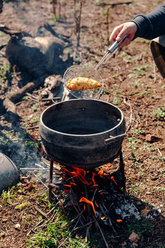 Unrecognizable cook preparing delicious pasty in boiling oil in pot on camping fire in countryside
