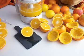 juicer with orange juice, whole and squeezed oranges lie on the table