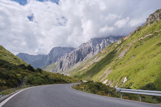 Curvy asphalt path leading through grassy hills covered with moss near calm peaks disappearing into distance