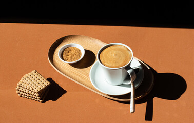From above of ceramic cup of tasty coffee near crunchy crackers on wooden plate near bowl with cane sugar in cafe in sunlight