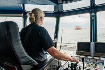 Captain of deck Officer on bridge of vessel or ship during navigaton watch at sea . He is maneuvering with cpp thrusters propulsion and bowthruster