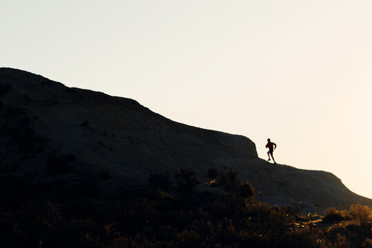 Side view silhouette of unrecognizable athlete running up on mountain slope during workout at sunset
