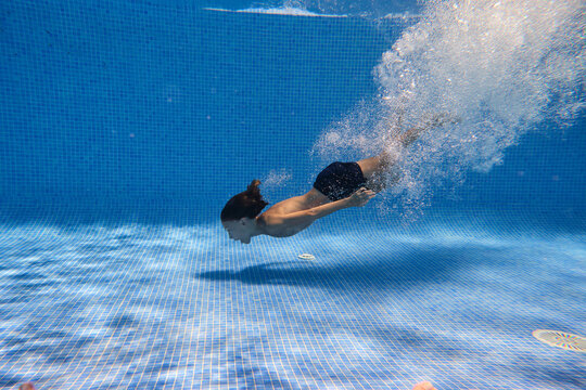Underwater shot full body energetic teenage boy in swimming trunks diving into clean pool water in resort