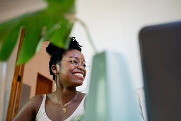 From below of young concentrated African American freelancer in casual clothing working on laptop at table with green pot plants