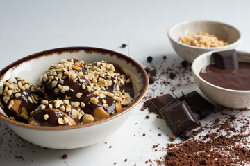 Presentation of delicious profiteroles with vanilla cream, chocolate sauce and hazelnut pieces.