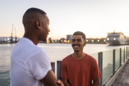 Smiling young ethnic friends spending time together on river embankment in evening