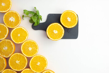 on the table, cut oranges near mint leaves and an orange cut in half on a plate