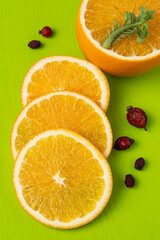 Sliced orange and dried rose hips on a green cutting board