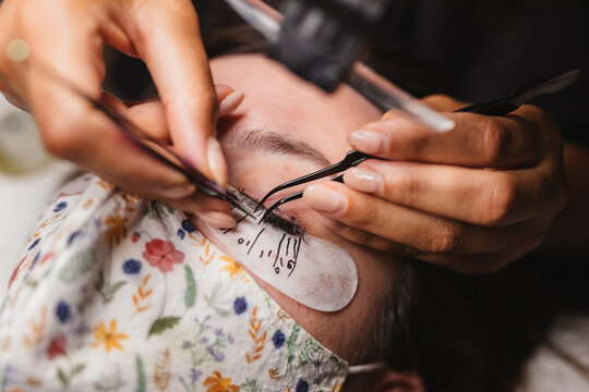 From above of crop anonymous master doing eyelash extension after mapping for unrecognizable female customer in face mask