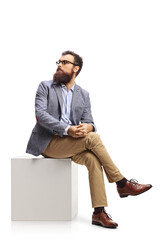Bearded man sitting on a white cube and looking behind