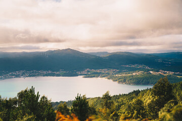 Scenic view of calm pond surrounded by mountains under cloudy sky at sunset