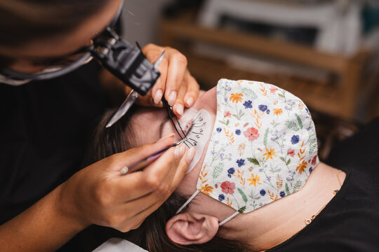 From above of crop anonymous master doing eyelash extension after mapping for unrecognizable female customer in face mask