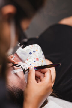 From above of crop anonymous master doing eyelash extension after mapping for unrecognizable female customer in face mask